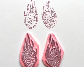 May include: Two pink rubber stamps with dragon fruit designs. One stamp shows a dragon fruit with its skin on, the other shows a dragon fruit with its skin removed.