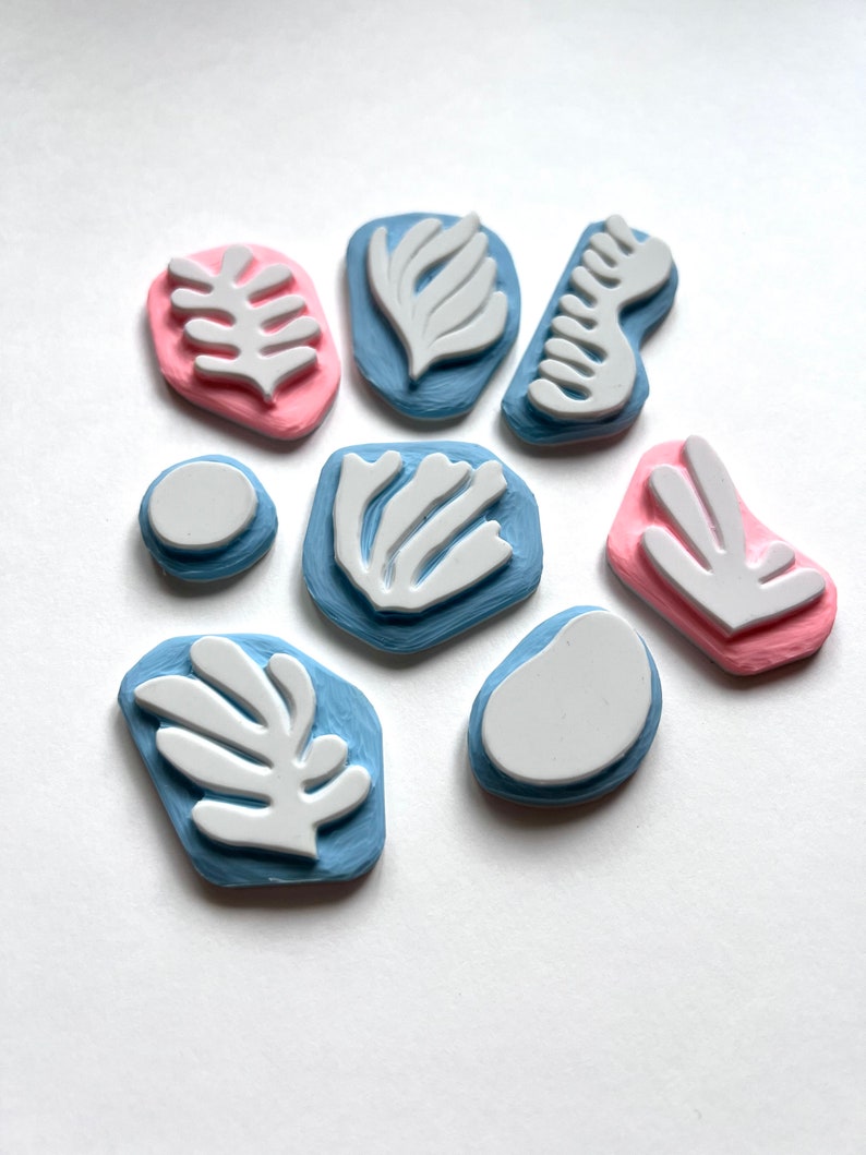 K&ouml;nnte beinhalten: Satz von neun Gummistempeln mit abstrakten Blatt- und geometrischen Formen. Die Stempel sind in Blaut&ouml;nen und Rosa.