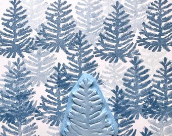 May include: A light blue rubber stamp shaped like a pine tree. The stamp is on a white background with a pattern of blue pine trees.