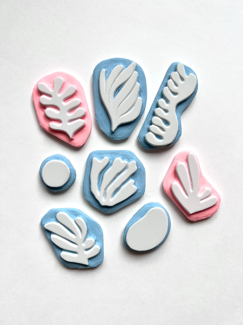 K&ouml;nnte beinhalten: Ein Satz von acht Stempeln aus Gummi mit abstrakten Blatt- und Blumenmotiven. Die Stempel sind in verschiedenen Formen und Gr&ouml;&szlig;en, einige sind rosa und andere blau.