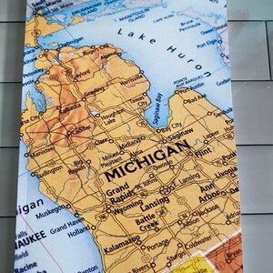 May include: A notebook featuring a detailed map of Michigan, with cities and roads. The cover displays a vintage aesthetic with a yellow, brown, and blue color scheme. The word "MICHIGAN" is prominently displayed.
