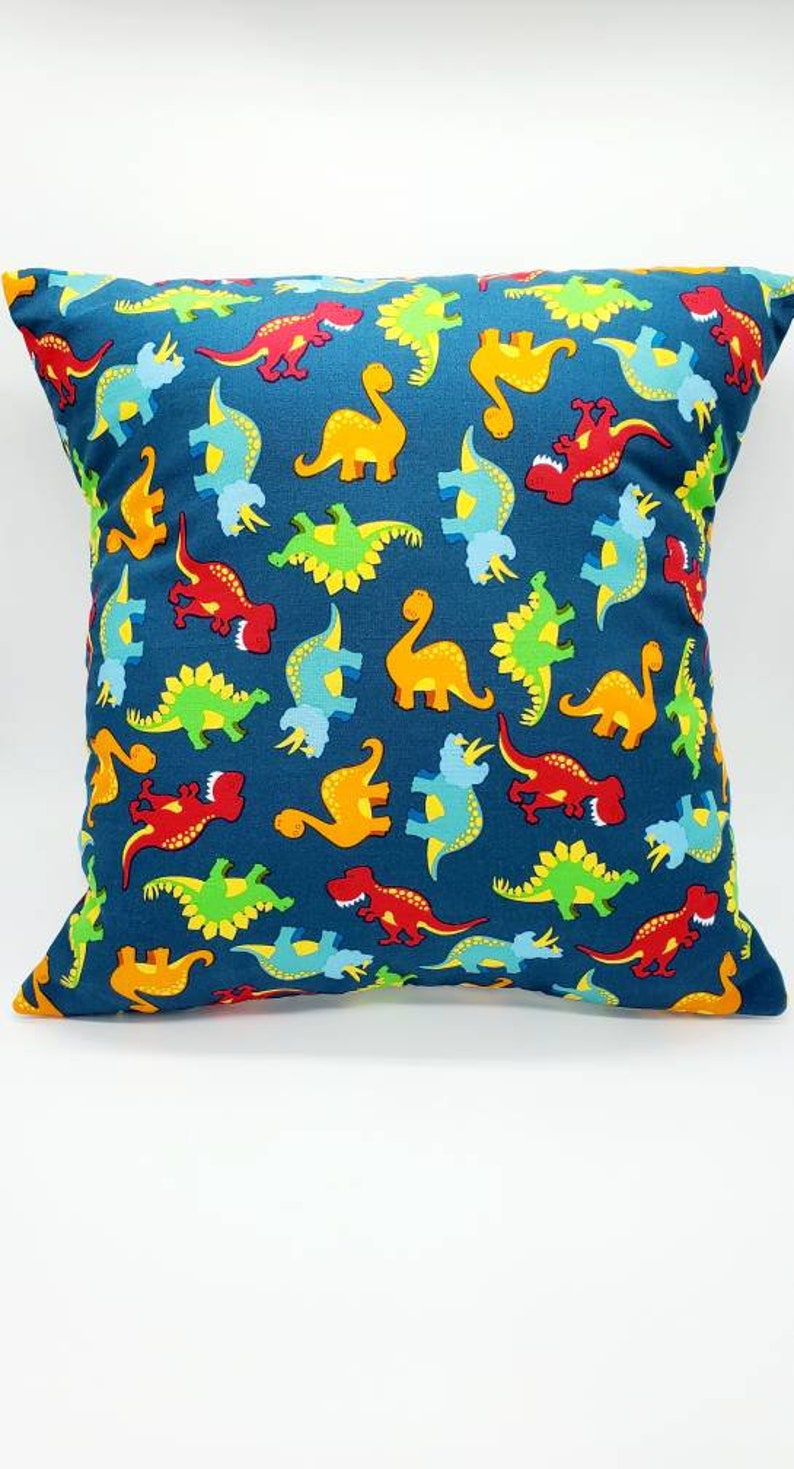 May include: A blue pillow with a pattern of colorful dinosaurs. The dinosaurs are in various poses, including standing, walking, and running. The pillow is made of a soft, comfortable fabric.