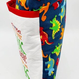 May include: A white pillow with red trim and a blue fabric back featuring a repeating pattern of colorful dinosaurs. The front of the pillow has the text "You are stronger than you think, about it, you are magic, just let you, be you".