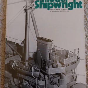 May include: A vintage issue of "Model Shipwright" magazine. The cover features a detailed black and white image of a ship model. The magazine title is in green and the issue number is 21. The magazine is on a textured surface.