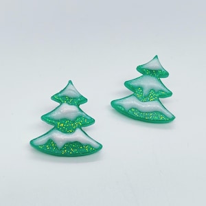 May include: Two green glitter Christmas tree earrings with white snow accents.