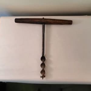 May include: A vintage wooden handled drill bit with a metal twist drill bit. The drill bit is on a white surface.