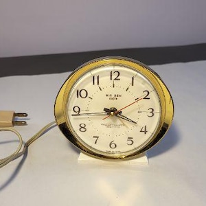 May include: A white ceramic mug with a black handle and the text "But First, Coffee" in a bold, black font. The mug is set against a neutral background, highlighting its simple design.
