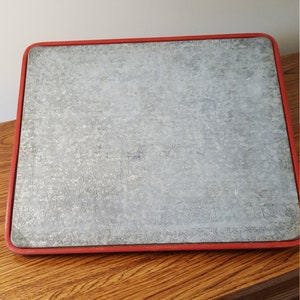 May include: A gray metal cutting board with a red rim. The board is sitting on a wooden surface.