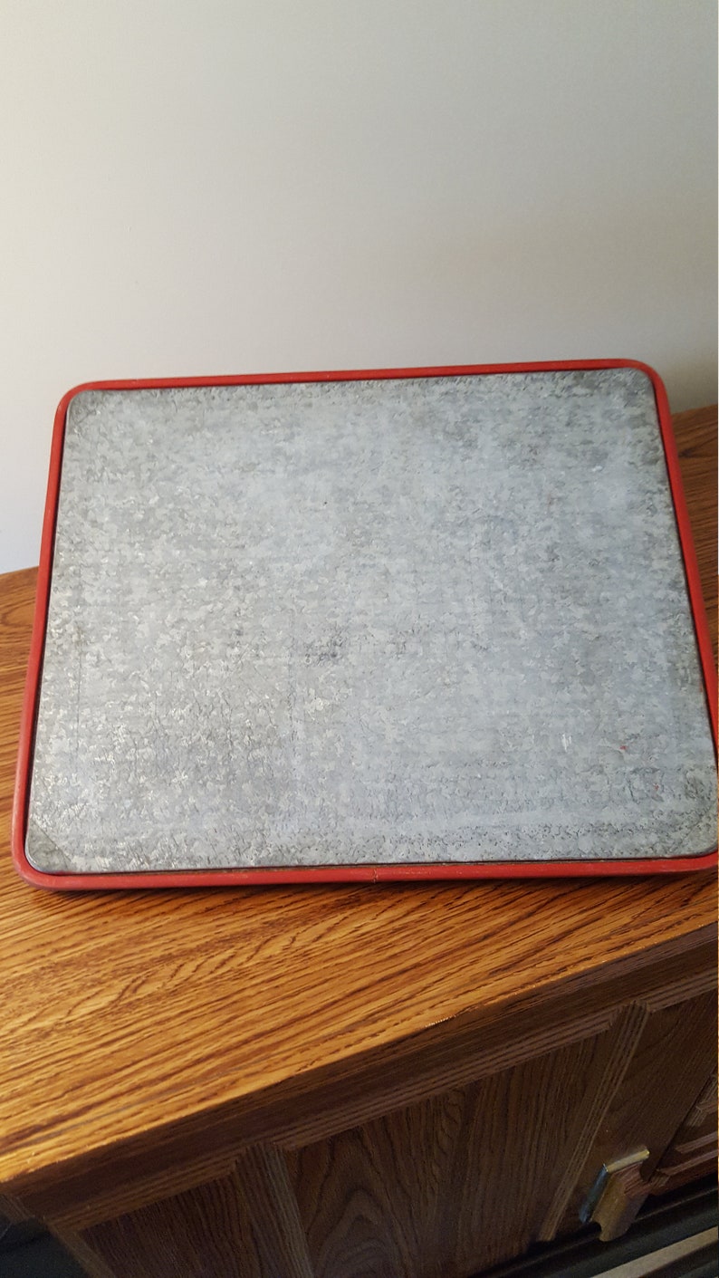 May include: A gray metal cutting board with a red rim. The board is sitting on a wooden surface.