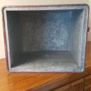 May include: A vintage metal ice chest with a red trim and a galvanized interior. The chest is empty and ready to be filled with ice and drinks.