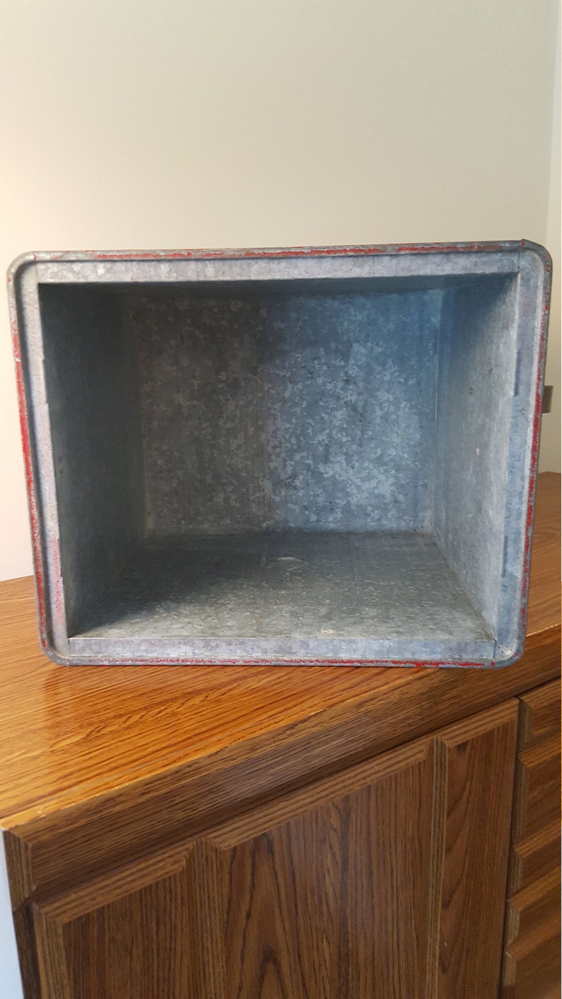 May include: A vintage metal ice chest with a red trim and a galvanized interior. The chest is empty and ready to be filled with ice and drinks.