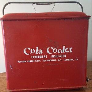 May include: Red vintage cooler with a metal handle and the text "Cola Cooler Fiberglass Insulated Poloron Products Inc. New Rochelle, N.Y. Scranton, Pa."