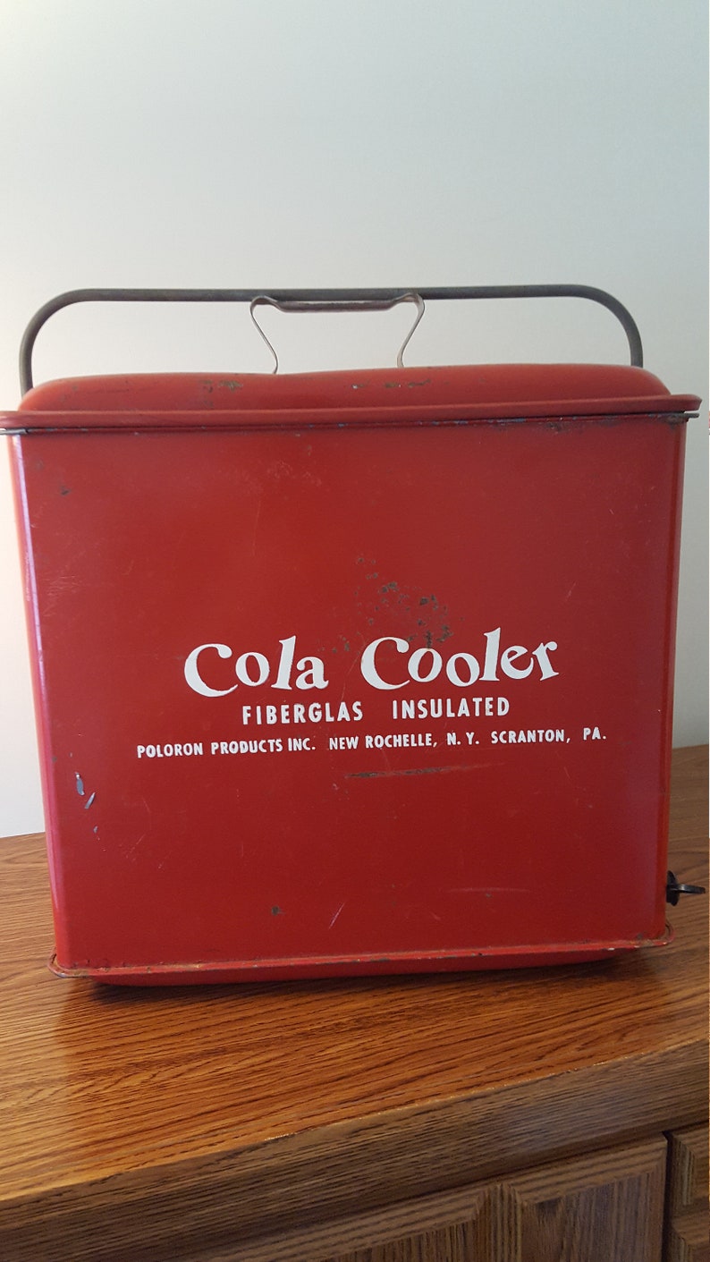 May include: Red vintage cooler with a metal handle and the text "Cola Cooler Fiberglass Insulated Poloron Products Inc. New Rochelle, N.Y. Scranton, Pa."
