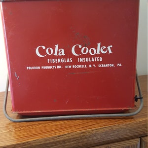 May include: Red metal cooler with a white "Cola Cooler" logo and the text "Fiberglass Insulated" and "Poloron Products Inc. New Rochelle, N.Y. Scranton, PA."