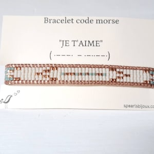 May include: A white and rose gold beaded bracelet with a blue accent. The bracelet spells out "JE T'AIME" in morse code.