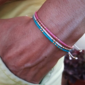Può includere: Un set di tre braccialetti con perline rosa, bianche e turchesi. I braccialetti sono realizzati con piccole perline rotonde e hanno un aspetto delicato e femminile.
