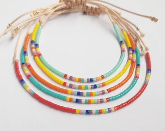 May include: Five colorful beaded bracelets with a macrame closure. The bracelets feature a variety of colors, including red, orange, yellow, turquoise, and blue, with small, colorful beads. The bracelets are connected by a beige macrame knot.