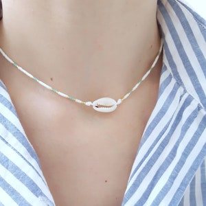 May include: A white and light blue beaded necklace with a small white seashell pendant.