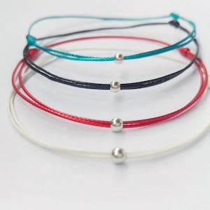 Peut inclure: Quatre bracelets avec des perles argentées. Les bracelets sont blancs, rouges, noirs et turquoise.