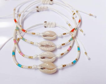 May include: Four white cord bracelets with seashell charms. Each bracelet features colorful beads in red, pink, blue, and gold accents. The bracelets are adjustable and tied with a knot.
