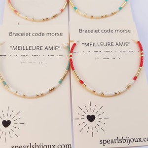 Peut inclure: Deux bracelets avec des perles blanches, dorées et rouges ou turquoise. Les bracelets sont sur des cartes avec le texte "Bracelet code morse" et "MEILLEURE AMIE" en français. Les cartes ont également un cœur avec des rayons de lumière autour et l'adresse du site web "spearlsbijoux.com".