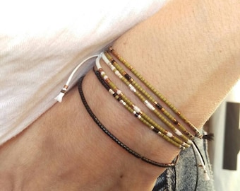 May include: A set of five beaded bracelets in shades of green, white, and brown. The bracelets are tied together with a white cord.