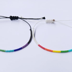 Peut inclure: Deux bracelets d'amitié arc-en-ciel, l'un avec un cordon noir et l'autre avec un cordon blanc.