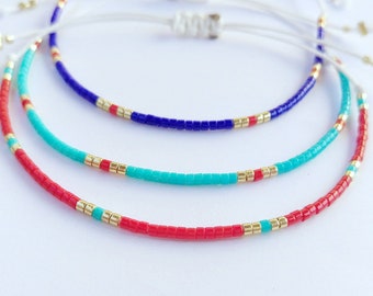 May include: Three beaded bracelets in red, turquoise, and blue with gold accents. The bracelets are layered on top of each other.