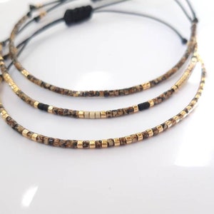 Peut inclure: Trois bracelets superposés avec de petites perles dorées et brunes, et des perles noires sur la couche du milieu.