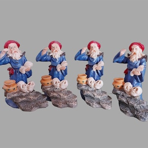 Könnte beinhalten: Vier Zauberer-Figuren mit roten Hüten und blauen Roben. Jede Figur steht auf einem felsigen Sockel mit einem Totenkopf, einem kleinen Topf und einer Schriftrolle. Die Zauberer haben weiße Bärte und gestikulieren.