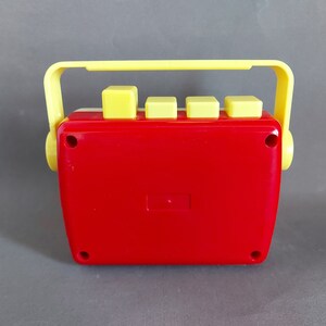May include: A red and yellow toy cassette player with a handle on top. The player has four yellow buttons on the front.