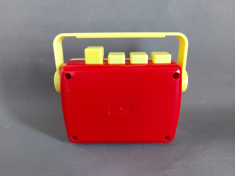 May include: A red and yellow toy cassette player with a handle on top. The player has four yellow buttons on the front.