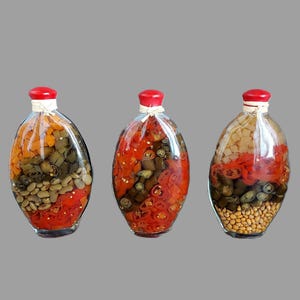 May include: Three glass bottles with red lids filled with a variety of pickled vegetables, including red peppers, green peppers, and beans.