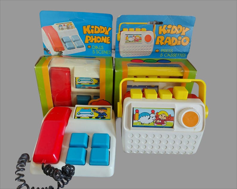 May include: Two vintage toy sets, a red and white toy phone with a black cord and a white toy radio with a yellow handle. The phone has a picture of a car and a police officer on the front. The radio has a picture of a sheep and a girl on the front. Both toys have the words "Kiddy Phone" and "Kiddy Radio" on the packaging.