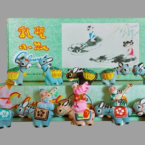 Peut inclure: Un ensemble de 10 figurines d'ânes colorées avec des cavaliers, emballées dans une boîte avec des caractères chinois et le mot "Coloured" imprimé dessus. Les ânes sont peints dans des tons de bleu, vert, jaune, rouge et blanc, et chaque cavalier est habillé d'une tenue colorée différente.