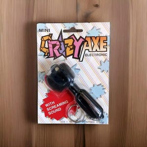 May include: A black plastic keychain shaped like an axe with a red handle. The keychain is labeled "Mini Crazy Axe Electronic" and "With Screaming Sound".