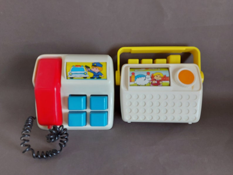 May include: Two vintage toy phones with a white base and colorful accents. One phone has a red receiver and blue buttons, and the other has a yellow handle and an orange button. Both phones feature cartoon images.