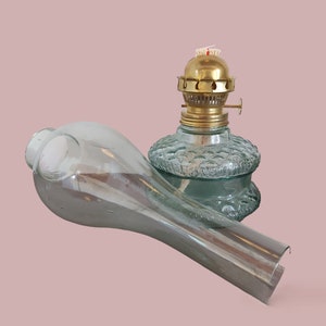 May include: A vintage oil lamp with a clear glass chimney and a brass top. The lamp is made of green glass with a textured surface.