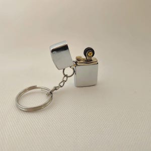 May include: A silver lighter keychain with a flip top and a small ring for attaching to keys.