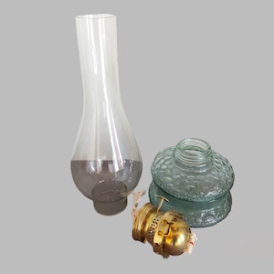 May include: A set of three glass lamp parts, including a clear glass chimney, a green glass globe with a textured surface, and a brass burner.