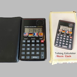 May include: A black talking calculator and alarm clock with a black leather case. The calculator has a digital display showing the time 1-34-07 and a row of flags representing different languages. The calculator has buttons for numbers, operations, and functions like TM, ALM, SET, and ON. The box for the calculator is white with the text "Talking Calculator/Alarm Clock" printed in red and black.