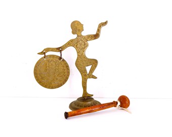 May include: A brass gong with a decorative design, a wooden mallet, and a brass figurine of a dancer holding the gong.