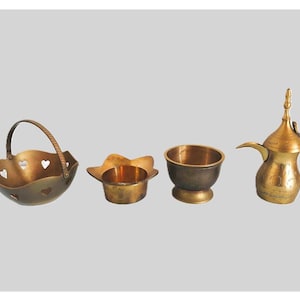 Puede incluir: Cuatro recipientes de metal de color dorado, que incluyen un tazón pequeño, una taza pequeña, una cesta con asa y una cafetera árabe tradicional con un pico y un asa.