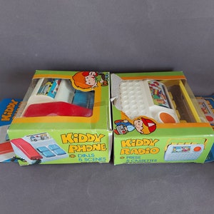 May include: Two vintage toy boxes with Kiddy Phone and Kiddy Radio on the front. The phone is red and white with a dial and the radio is white and yellow with a cassette player. Both boxes have cartoon characters on them.