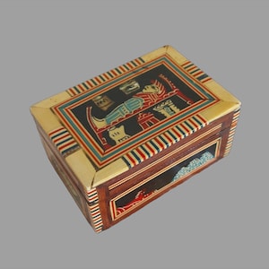 May include: A small wooden box with an intricate design. The box is decorated with colourful stripes and an image of an Egyptian figure holding a jar. The box is made of wood and has a hinged lid.