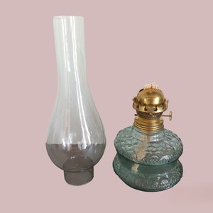 May include: A clear glass oil lamp chimney and a green glass oil lamp with a brass top and wick.