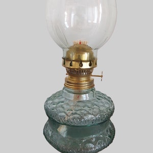 May include: A vintage oil lamp with a clear glass globe and a textured green glass base. The lamp has a brass wick holder and a brass cap.