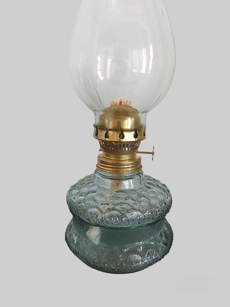 May include: A vintage oil lamp with a clear glass globe and a textured green glass base. The lamp has a brass wick holder and a brass cap.