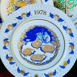 Op de afbeelding: Een witte keramische kerstplaat met een blauw en gouden ontwerp. De plaat toont een scène met herders en schapen met een ster aan de hemel. Het jaar 1978 is in goud op de plaat gedrukt.