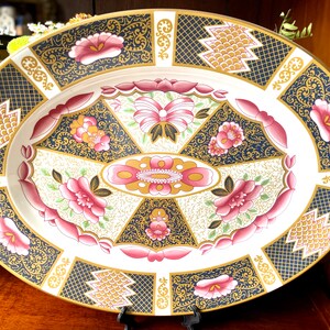 Peut inclure: Un plat de service ovale avec un fond blanc et un motif décoratif en or, noir et rose. Le motif présente des motifs floraux, des motifs géométriques et un médaillon central.